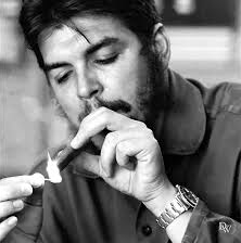 Che Guevara acende um charuto com um fósforo. Em seu pulso, vê-se o seu famoso Rolex.