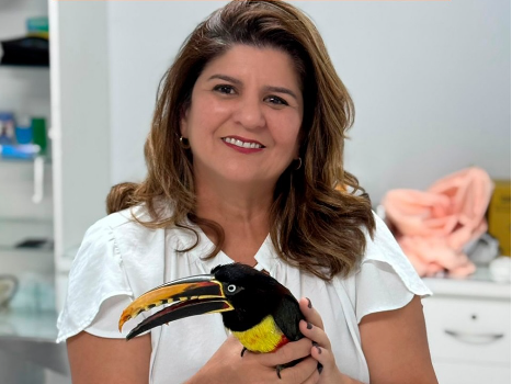 A vereadora de Ji-Paraná-RO, Dra Rosana, com roupa branca, em uma sala branca e segurando um tucano.