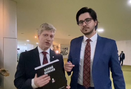 O deputado Marcel van Hattem segura o Dossiê Moraes com o vereador Rodrigo Marcial ao lado no Congresso Nacional.